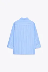 Camisa celeste a rayas verticales blancas, de cuello solapa y manga tres cuartos. Tiene aberturas laterales en el ruedo y cierre frontal con botones ocultos.