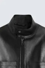 Cazadora cropped de piel negra, con cuello alto, cierre frontal con cremallera, bolsillos de parche en el pecho y puños con botón.