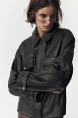 Cazadora negra de cuero con cuello solapa, manga larga con trabilla y bolsillos de parche con solapa en el delantero. Cierre frontal con cremallera y botones a presión ocultos por solapa.