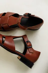 Sandalia roja de cuero vacuno con diseño de tiras entrecruzadas y hebilla lateral. Tiene suela de cuero artesanal y taco bajo.