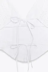 Top blanco tipo corsetero con escote pico y tirantes anchos. Detalle de bordados perforados a tono. Abertura en espalda ajustable con lazadas.