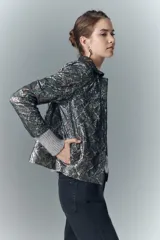 Camisa de cuero ovino con estampado de piel de serpiente multicolor y detalles metalizados. Presenta un cuello alto, botones a presión con logo de alas y puños de tejido de punto gris.