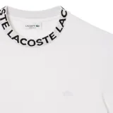 Remera blanca de corte clásico con cuello redondo y mangas cortas. El cuello presenta la inscripción "Lacoste" en negro.