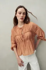 Blusa estampada celeste y blanca de caída fluida con cuello redondo y lazos frontales. Diseño con cortes horizontales y frunces, mangas largas con puños elastizados.