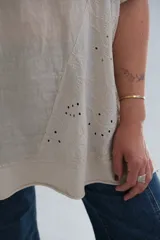 Blusa beige de lino con detalle de bordado floral y perforaciones en el lateral.