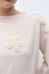 Sweater de tejido punto color beige melange, con cuello redondo y apliques de flores de crochet en relieve sobre los hombros y el pecho.