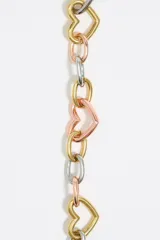 Pulsera de cadena metálica con eslabones en dorado, plateado y cobre. Incluye dijes de corazones y un dije redondo con el logo de la marca grabado.