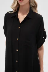 Vestido camisero midi negro de corte holgado, con cuello camisero, mangas cortas con trabillas, cierre frontal con botones, bolsillo en el pecho y bolsillos laterales.