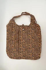 Tote bag de tela con estampado de hojas de palmera en tonos azul, celeste y rosa. Tiene doble asa superior y cierre con botón a presión.