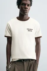 Camiseta color crudo de corte relaxed fit, con cuello redondo y mangas cortas con ribete marrón. Estampado frontal con la frase "Golden Hour" en color marrón.