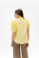 Camisa de lino color lila con volados en el cuello y en las mangas cortas abullonadas. Presenta un diseño de corte recto con cierre frontal de botones.