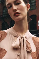 Vestido midi color beige con detalles de encaje marrón, cuello alto con lazo, escote pico, manga larga y botones frontales.
