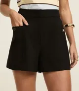 Short color beige de cintura alta, confeccionado en tejido plano con estructura sastre, con bolsillos laterales con tachuelas metalizadas.