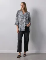 Camisa de mujer estampada con hojas en blanco y negro, cuello con solapa, abertura central con botones, bolsillos aplicados en el delantero y mangas largas con lazo.