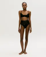 Conjunto de lencería negro de encaje, compuesto por un corpiño triangular con tirantes finos y una bombacha de tiro alto con paneles de encaje transparente.