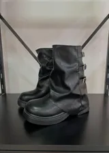 Botas de caña media negras de cuero sintético, con suela track y tres hebillas laterales.