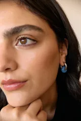 Aros de acero quirúrgico hipoalergénico con forma de argolla plateada y dije circular colgante de piedra natural color azul.