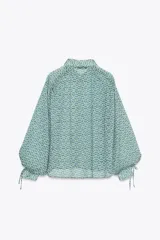 Camisa de manga larga con estampado floral en tonos verde y azul. Tiene cuello solapa, cierre frontal con botones y lazadas en los puños.