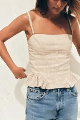Top corto de escote recto y tirantes finos, con estampado de cuadros vichy en tonos beige y blanco. Presenta tejido elástico tipo nido de abeja en la espalda, detalle de botones forrados en el delantero y bajo con volantes. Cierre con cremallera lateral oculta en la costura.