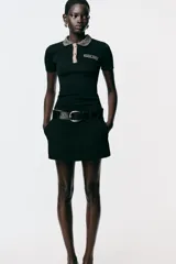 Chomba negra de corte slim fit, con cuello polo y mangas cortas. Presenta un falso bolsillo en el pecho y cierre frontal con botones. Detalle de hilo metalizado en cuello, bolsillo y tapeta.