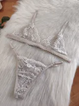 Conjunto de lencería color nude, compuesto por un bralette triangular de encaje floral con tirantes finos y una tanga regulable clásica de encaje a juego.