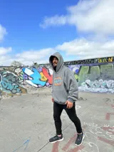 Canguro negro con capucha y cordones ajustables. Estampa en la espalda con el texto "Chema Surf Trip" y dibujos de un sol, una tabla de surf, una carpa y otros elementos relacionados con el surf.