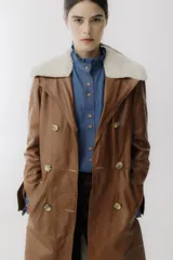 Trench de cuero color camel con cuello de piel sintética color crema, doble botonadura, bolsillos laterales y corte evasé.