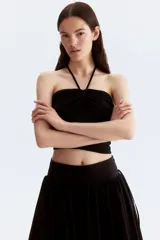 Top corto negro de punto con textura, corte entallado, escote halter y tiras finas con cuentas en los extremos.