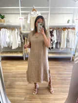 Vestido midi color beige confeccionado en lino, con escote en V y mangas cortas con detalle de flecos. Presenta aberturas laterales en el ruedo.