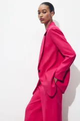 Blazer fucsia de cuello solapa y manga larga con hombreras. Detalle de tejido efecto arrugado. Bolsillos delanteros de vivo. Cierre frontal con un botón.
