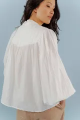 Camisa blanca de algodón con cuello mao, mangas largas abullonadas y costuras frontales.