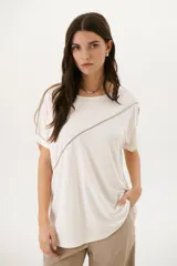 Remera negra de corte holgado con cuello redondo y mangas cortas con dobladillo. Presenta una línea diagonal blanca que cruza el frente desde el hombro hasta la cadera.