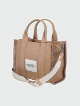 Bolso tipo tote pequeño de Marc Jacobs confeccionado en tejido jacquard color tostado. Presenta el texto 'THE TOTE BAG MARC JACOBS' bordado en el frente en contraste, asas de mano superiores y cintas laterales con inscripciones de la marca.