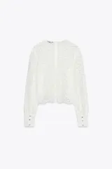 Top de encaje blanco con cuello redondo, mangas largas abullonadas y puños con botones metálicos.