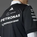 Camiseta negra de manga corta con cuello redondo, con logos de Mercedes AMG Petronas F1 Team y sponsors estampados en el frente y las mangas. Presenta las tres rayas blancas de Adidas en los hombros.