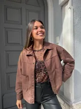 Chaqueta marrón de gamuza con cuello camisero, cierre frontal con botones y bolsillos de parche en el pecho.