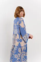 Vestido largo azul con estampado floral en tonos beige, confeccionado en viscosa. Presenta escote en V, botonadura completa en el frente y mangas largas con volados.
