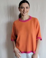 Buzo de punto color naranja con ribete rosa en cuello y mangas, de corte holgado y mangas cortas.