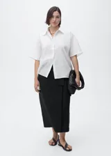 Camisa blanca de manga corta confeccionada en mezcla de algodón y lino, con cierre frontal de botones, cuello camisero y corte recto.