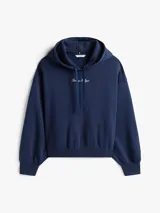 Buzo con capucha Tommy Hilfiger azul marino de corte amplio, confeccionado en tejido de felpa flexible de mezcla de algodón. Presenta logo texturizado en fuente script en el pecho, puños y bajo de punto canalé, cordón en la capucha y logo bordado en la manga.