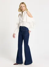 Pantalón de denim azul oscuro, corte acampanado, tiro alto, pretina con trabillas, cierre de botón y cremallera, cuatro bolsillos, ribete vertical y pespuntes.