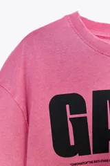 Camiseta rosa de algodón con efecto lavado, cuello redondo y manga corta. Estampado frontal con el texto "GAGA" en color negro.