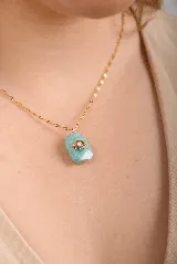 Collar con dije de piedra natural de jade color verde agua, con detalle de ojo turco en acero dorado. La cadena es de eslabones chatos en acero dorado.