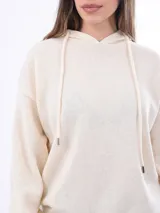 Canguro de tejido punto color crudo, con capucha y cordones ajustables. Presenta puños y cintura acanalados.