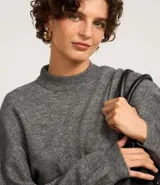 Suéter gris de punto, corte corto, con cuello alto y mangas largas abullonadas.