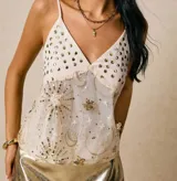 Top blanco con breteles finos, escote en V y apliques de lentejuelas doradas con forma de estrellas y lunas.