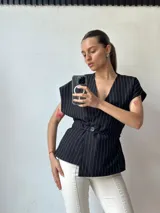 Chaleco negro con rayas verticales blancas, escote en V, corte ajustado y cierre cruzado con un botón. Sin mangas.