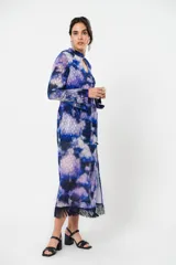 Vestido largo con estampado abstracto en tonos azules, violetas y grises. Tiene cuello mao con abertura en forma de gota, mangas largas acampanadas con detalle de botón en los puños, espalda abierta, tajo frontal y flecos en el ruedo.