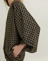 Blusa negra con estampado geométrico dorado, escote en V y mangas 3/4 amplias.
