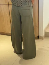 Pantalón ancho color verde oliva, de tiro alto y corte holgado. Confeccionado en mezcla de algodón y lino, con pinzas debajo de la rodilla, bordado de monograma en el bolsillo delantero y pespuntes a contratono.